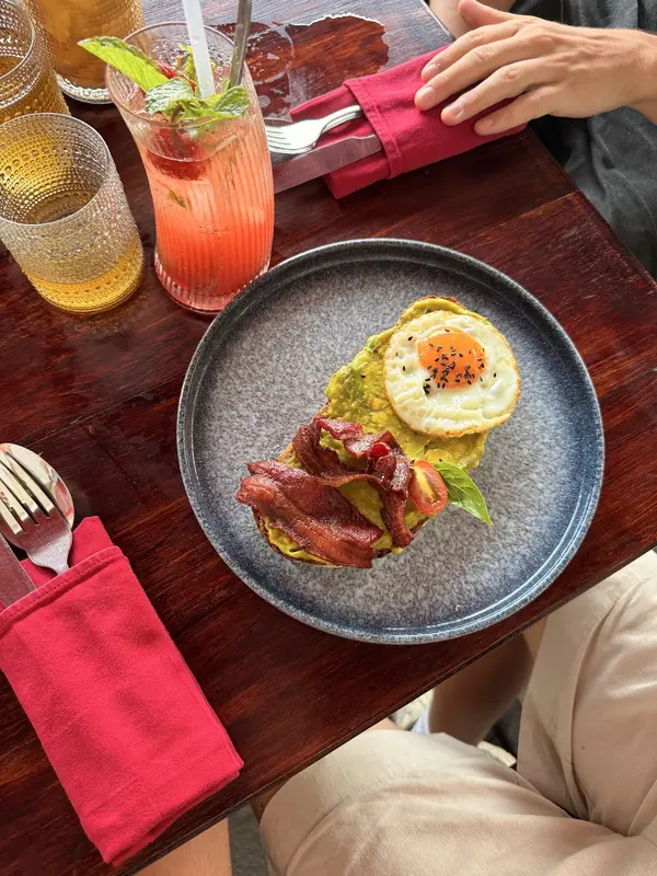 A breakfast plate with bacon, egg and avocado toast beside cold drinks